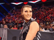 a woman in a spiked vest is smiling in front of a crowd at a raw show