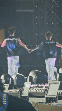two men are holding hands on a stage and one of them is wearing a shirt that says ' w dong dae ' on it