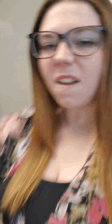 a woman wearing glasses and a floral top looks at the camera