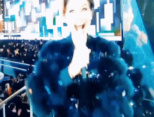 a woman in a blue fur coat is holding a microphone in front of a crowd of people