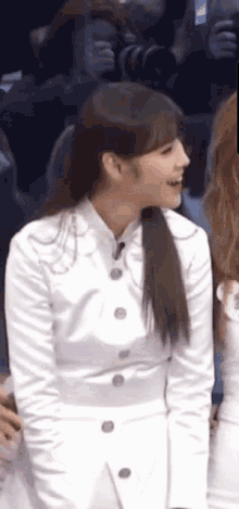 a woman in a white dress is sitting in front of a crowd and smiling .