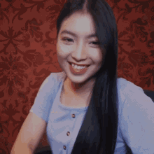a woman with long black hair is smiling in front of a red wallpaper