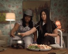 two women are sitting at a table with a plate of food on it