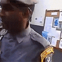 a police officer wearing a hat and glasses is standing in front of a wall with papers on it .