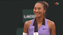 a woman wearing a purple nike tank top smiles in front of a tv screen