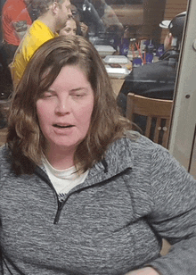 a woman sitting at a table with her eyes closed wearing a grey sweater