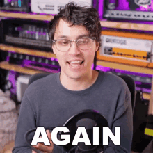 a man wearing glasses holds a microphone and says " again "