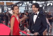a woman in a red dress is talking to a man in a suit on a red carpet