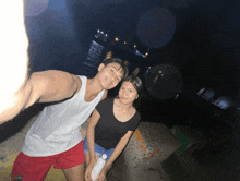 a man in a white tank top and red shorts stands next to a woman in a black t-shirt