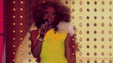 a drag queen is singing into a microphone in front of a wall of lights .