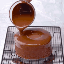 a chocolate cake is being covered in chocolate icing on a cooling rack