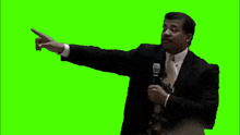 a man in a suit and tie is standing in front of a microphone and pointing .
