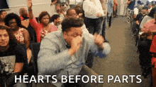 a man is sitting in front of a crowd with the words " hearts before parts " written above him