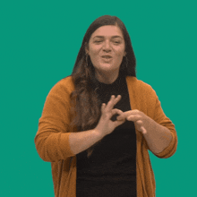 a woman wearing a yellow cardigan is smiling and making a thumbs up sign