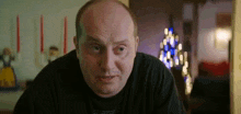 a bald man in a black shirt is looking at the camera .