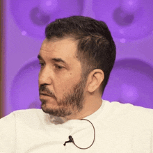 a man with a beard is wearing a white shirt with a microphone attached to it