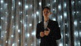 a man in a suit stands in front of a curtain with lights hanging from it