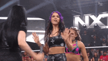 a woman with purple hair stands in front of a nxt logo