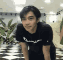 a young man wearing a black champion t-shirt is standing on his knees in a room .