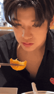 a man with a red heart on his shirt is eating a piece of food with chopsticks