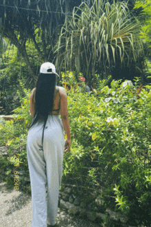 a woman wearing a white hat and grey sweatpants is standing in a garden