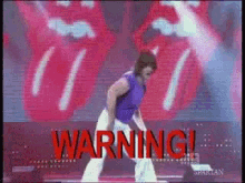 a man in a purple shirt is dancing on a stage in front of a rolling stones sign .