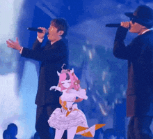 a man in a suit is singing into a microphone next to a girl in a white dress with horns .