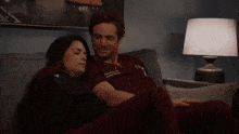 a man and woman are laying on a couch with a lamp in the background