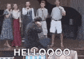 a group of people are standing on a stage with a man kneeling down in front of a microphone .