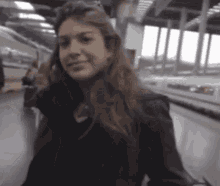 a woman in a black jacket is smiling while standing on a train platform
