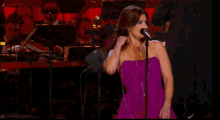 a woman in a purple dress sings into a microphone in front of an orchestra