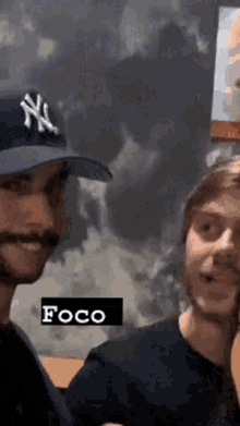 two men are standing next to each other and one of them is wearing a new york yankees hat .