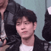 a young man wearing a black jacket and a white t-shirt is sitting in front of a microphone .