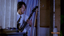 a man in a white shirt and tie is playing a guitar in front of a man laksa logo