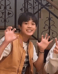 a young boy in a brown vest is smiling and making a funny face while standing in front of a staircase .