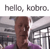 a man in a purple shirt is standing in a room with the words `` hello , kobro '' above him .