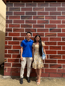 a man and a woman are posing in front of a brick wall