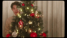 a young man stands in front of a christmas tree