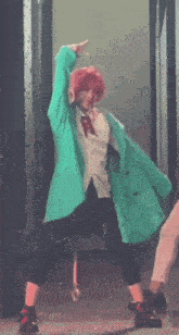 a person with pink hair and a green coat is dancing on stage .