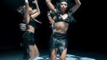 two women are dancing on a checkered floor in a dark room
