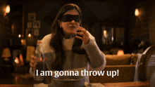 a woman wearing a blindfold throws up while sitting at a table