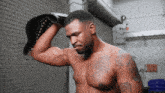 a shirtless man with a tattoo on his chest holds a boxing glove on his head