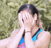 a woman covering her face with her hands in front of a bush