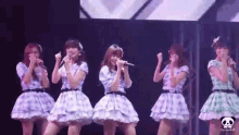 four girls singing into microphones on a stage with a panda logo in the corner