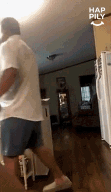 a man in a white shirt and blue shorts is dancing in a living room with the words hap pily written on the corner