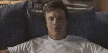a man in a white shirt is laying on a blue couch and smiling