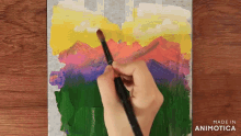 a hand is holding a brush and painting a mountain scene