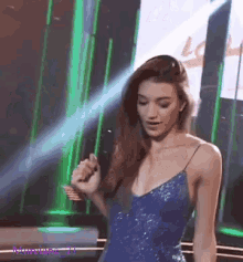 a woman in a blue dress is dancing on a stage with a green background