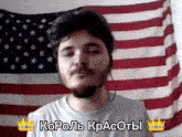 a man with a beard stands in front of an american flag and says " король красоты " in russian