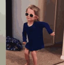 a little girl in a blue dress and sunglasses is dancing .